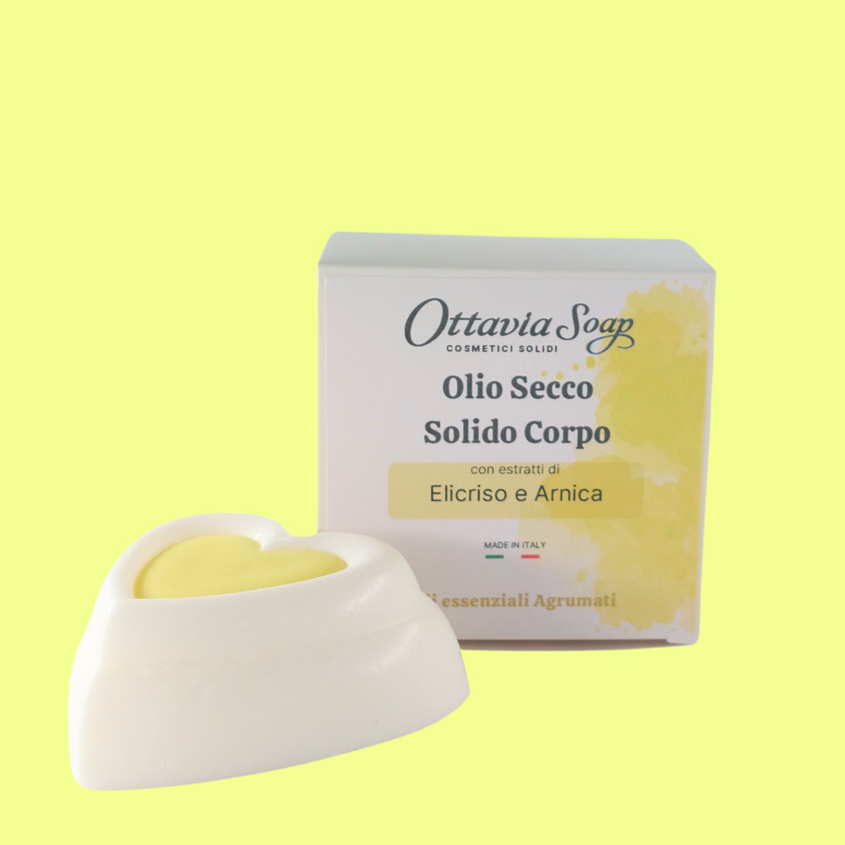 Olio secco solido con estratti di elicriso e arnica In primo piano un panetto bianco a forma di cuore ed in secondo piano la confezione con l’etichetta descrittiva