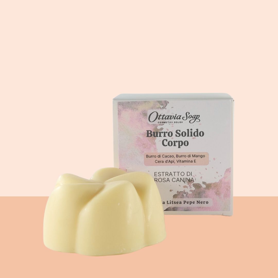 Burro Solido con estratti di Rosa Canina In primo piano un panetto bianco a forma di fiore . In secondo piano una scatolina in cartoncino bianco con stampati i dettagli del prodotto. Lo sfondo è color rosa salmone