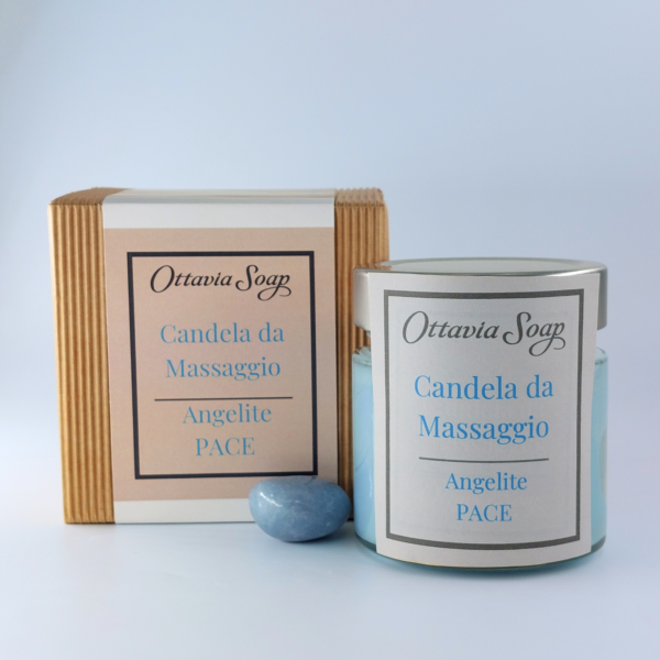 In primo piano un vasetto di vetro della candela da massaggio color azzurro. Di fianco al vasetto una pietra di Angelite. Sullo sfondo un cofanetto colora Avana chiuso con una fascia contenente le informazioni ed il nome del prodotto.
