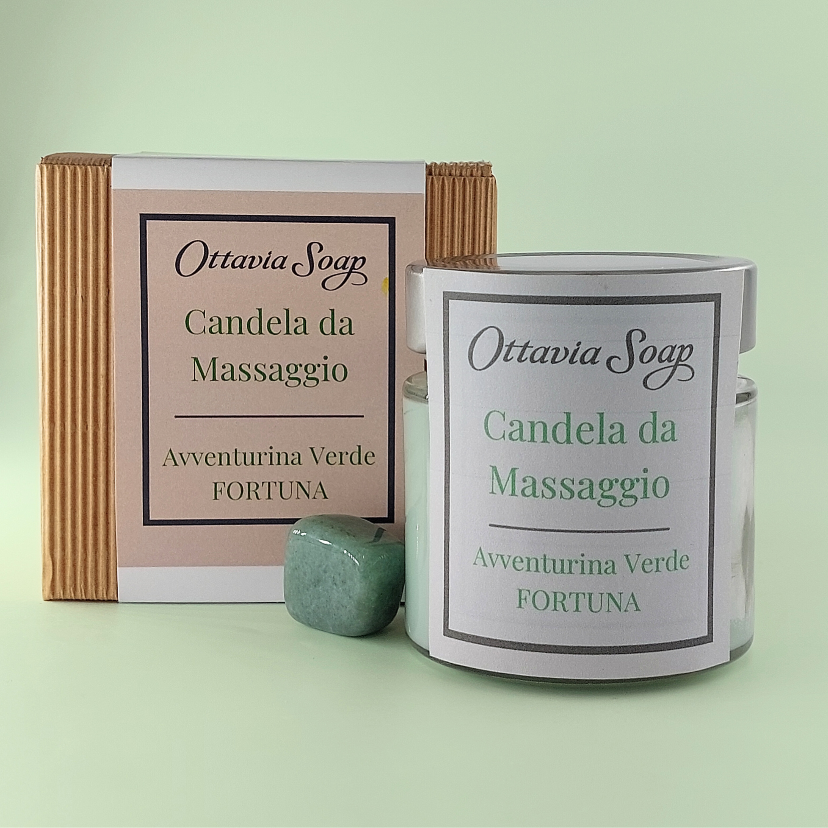 Candela Olio di Gerne di Grano e Pietra Avventurina Verde In primo piano un vasetto di vetro della candela da massaggio color giallo. Di fianco al vasetto una pietra di Avventurina Verde. Sullo sfondo un cofanetto color Avana chiuso con una fascia contenente le informazioni ed il nome del prodotto.