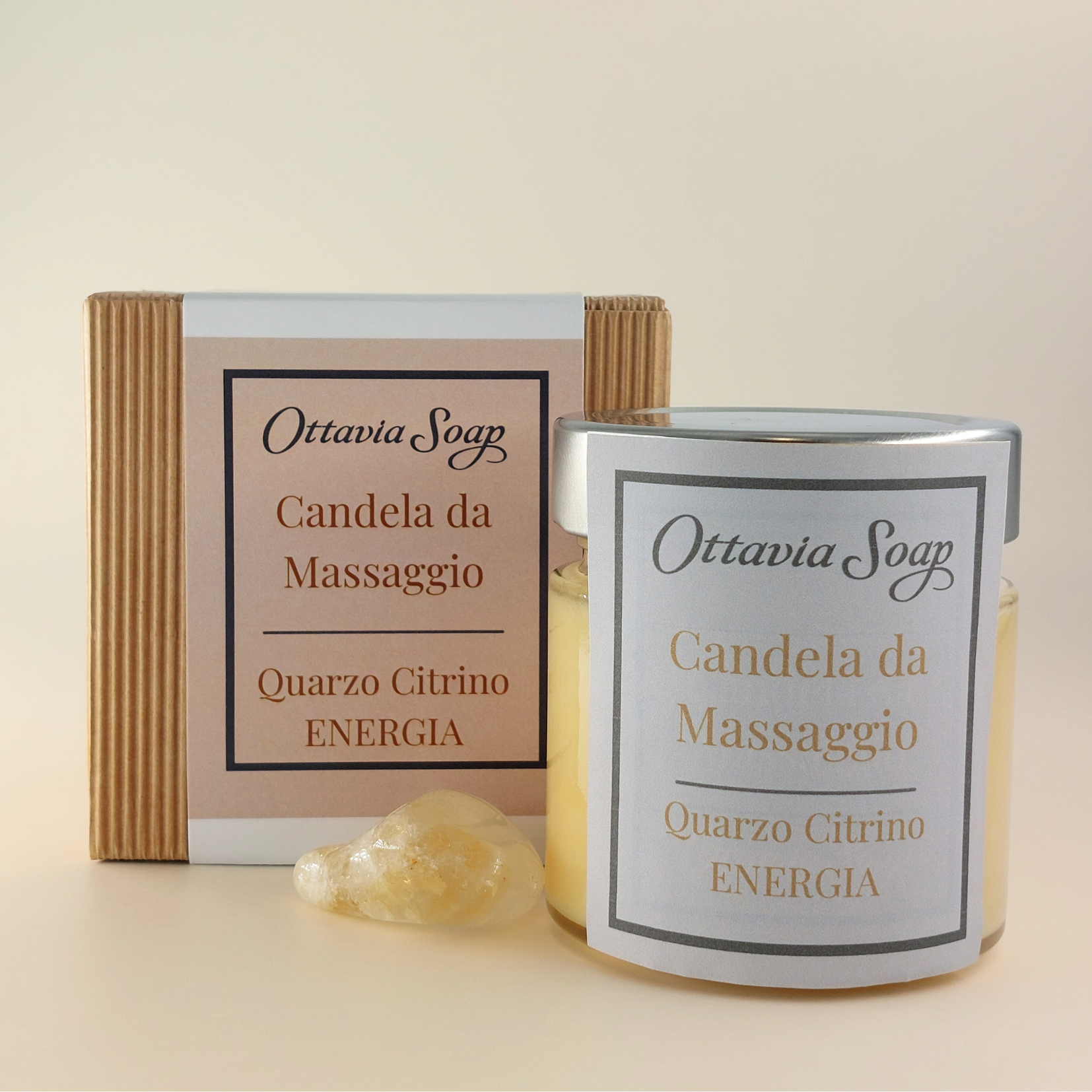 Candela Olio Macadamia e Pietra Quarzo Citrino In primo piano un vasetto di vetro della candela da massaggio color giallo. Di fianco al vasetto una pietra di Quarzo Citrino. Sullo sfondo un cofanetto colora Avana chiuso con una fascia contenente le informazioni ed il nome del prodotto.