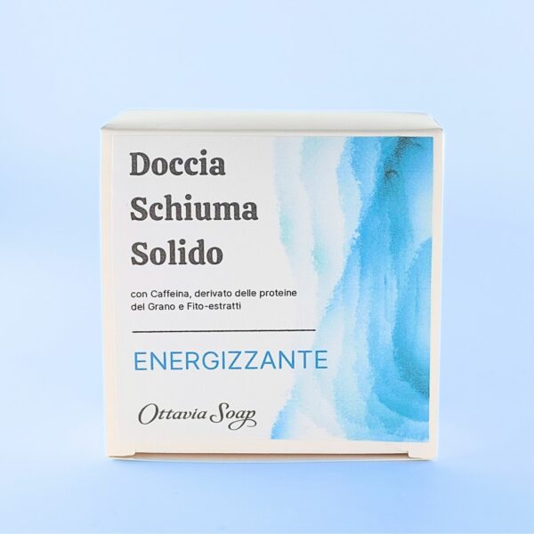 Scatolina quadrata in cartoncino bianco posta in verticale. Sul lato frontale una immagine composta da grafica colore Azzurro sfumata sul lato destro. Dalla parte sinistra il seguente testo: Doccia Schiuma Solido Energizzante con Caffeina