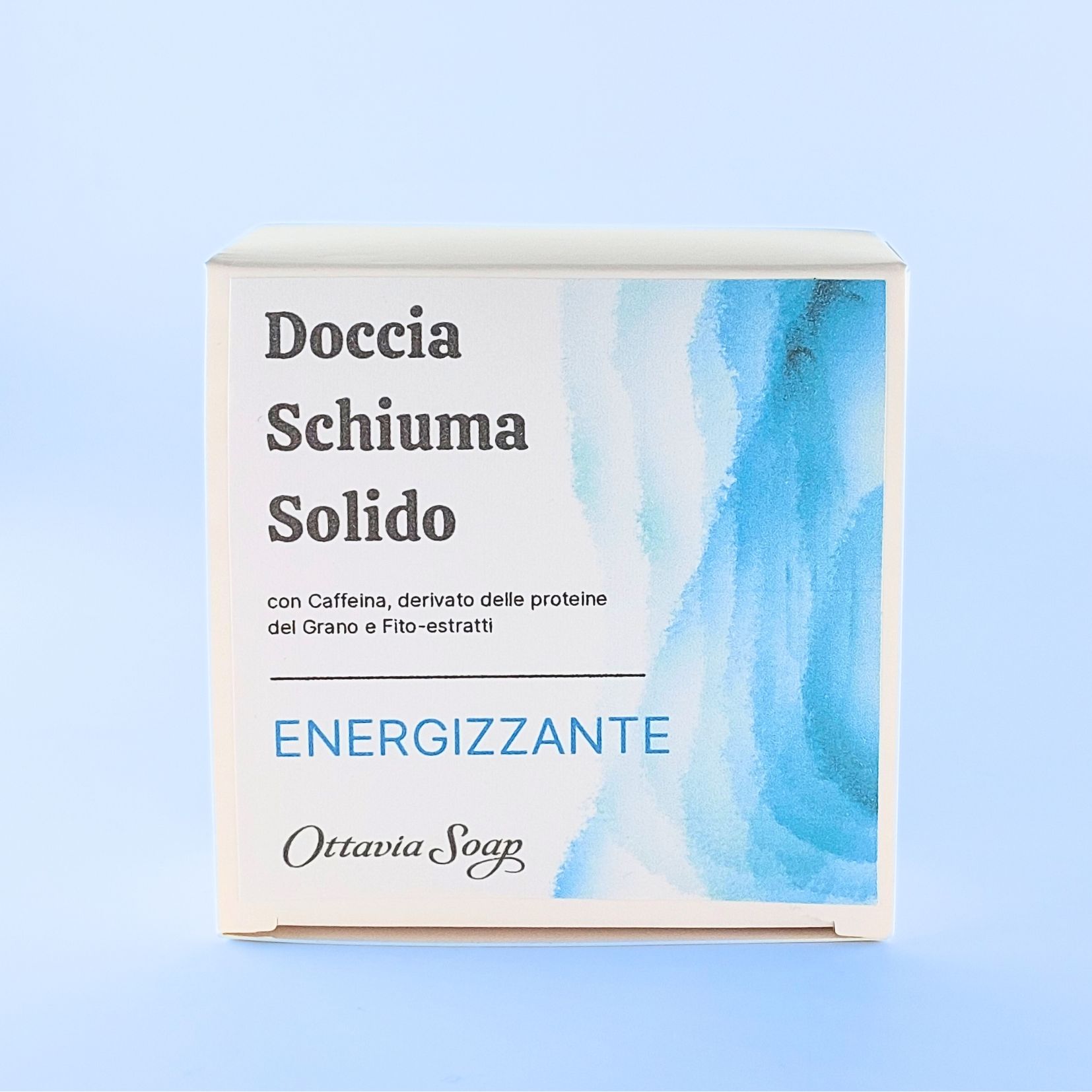 Doccia Schiuma Solido Energizzante Scatolina quadrata in cartoncino bianco posta in verticale. Sul lato frontale una immagine composta da grafica colore Azzurro sfumata sul lato destro. Dalla parte sinistra il seguente testo: Doccia Schiuma Solido Energizzante con Caffeina