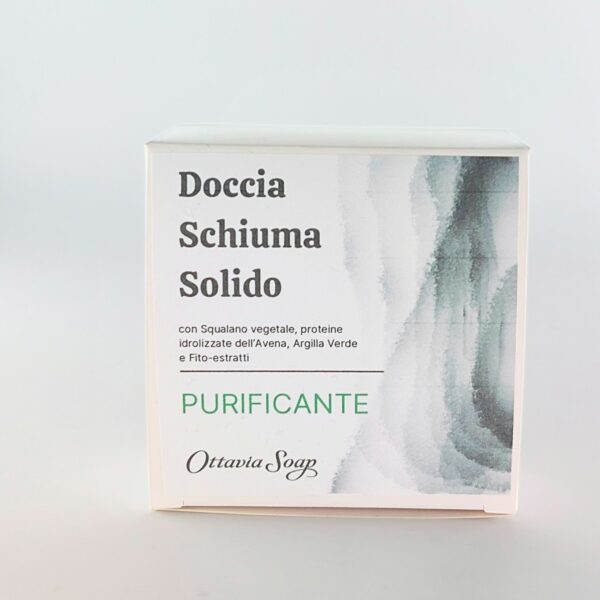 Scatolina quadrata in cartoncino bianco posta in verticale. Sul lato frontale una immagine composta da grafica color grigio chiaro e grigio scuro sfumata sul lato destro. Dalla parte sinistra il seguente resto: Doccia Schiuma Solido Purificante con Squalano