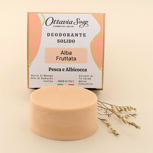 In primo piano un panetto ovale di deodorante solido color Albicocca. In secondo piano la confezione del deodorante con ii nome del prodotto e gli ingredienti in evidenza
