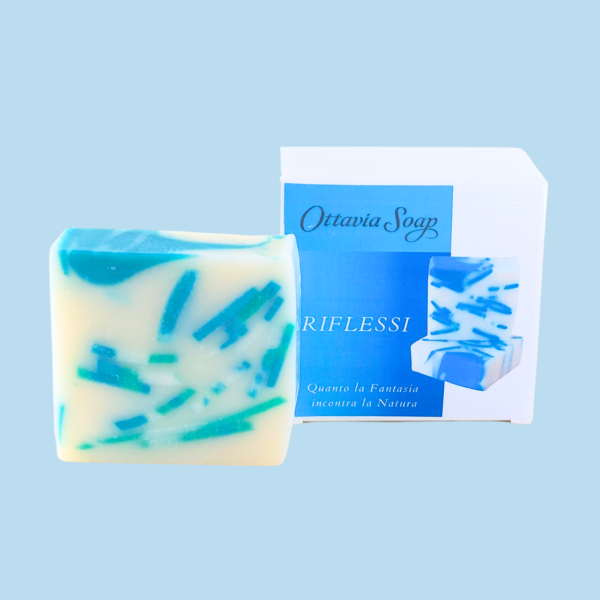 a sinistra, saponetta quadrata con macchie di colore blu-turchese su sfondo bianco. A destra Scatola cartoncino bianco con grafica blu e bianca